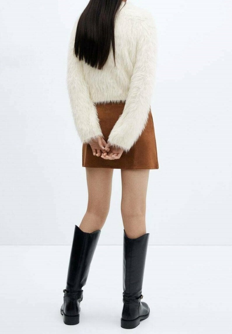 Biały futrzany sweter w wersji cropped, brązowa zamszowa mini spódniczka oraz wysokie czarne skórzane botki z detalem klamry. Widok z tyłu.