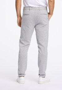 Pantalons de survêtement gris avec une coupe cintrée, une taille élastique, deux poches arrière et associés à des baskets blanches. La texture du tissu est lisse.