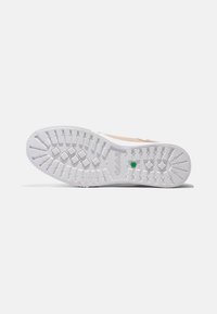 Schuhsohle aus weißem Gummi mit strukturierten Grip-Mustern und einem grünen Akzent. Abgerundete Zehenpartie und robuste Bauweise.
