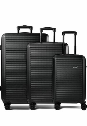 Tre valigie rigide nere con righe orizzontali, maniglie telescopiche estese e quattro ruote girevoli, disposte per dimensione dalla più grande alla più piccola.