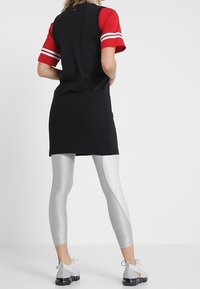 Robe noire et rouge à manches courtes avec des rayures blanches, accompagnée de leggings argentés et de chaussures de sport noires avec une semelle texturée.