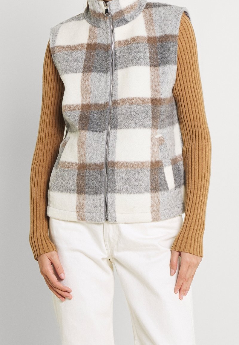 Fleece-Weste mit hohem Kragen im Karomuster in Grau, Braun und Creme, vorne geöffnet, getragen über einem gerippten Pullover.