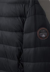 Zwarte gewatteerde jas mouw met een ronde Napapijri logo patch in zwart en oranje, met een wereldbol en tekst.