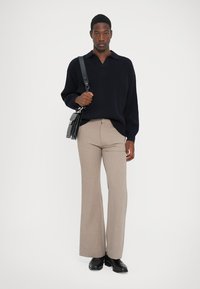 Navy ribbed sweater with a V-neck, beige wide-leg trousers, and black shoes. Black shoulder bag with a strap. Minimalist design.