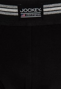 Mutande nere in cotone con una cintura elastica intrecciata caratterizzata da due strisce bianche. Include un'etichetta con la scritta "JOCKEY USA Originals."