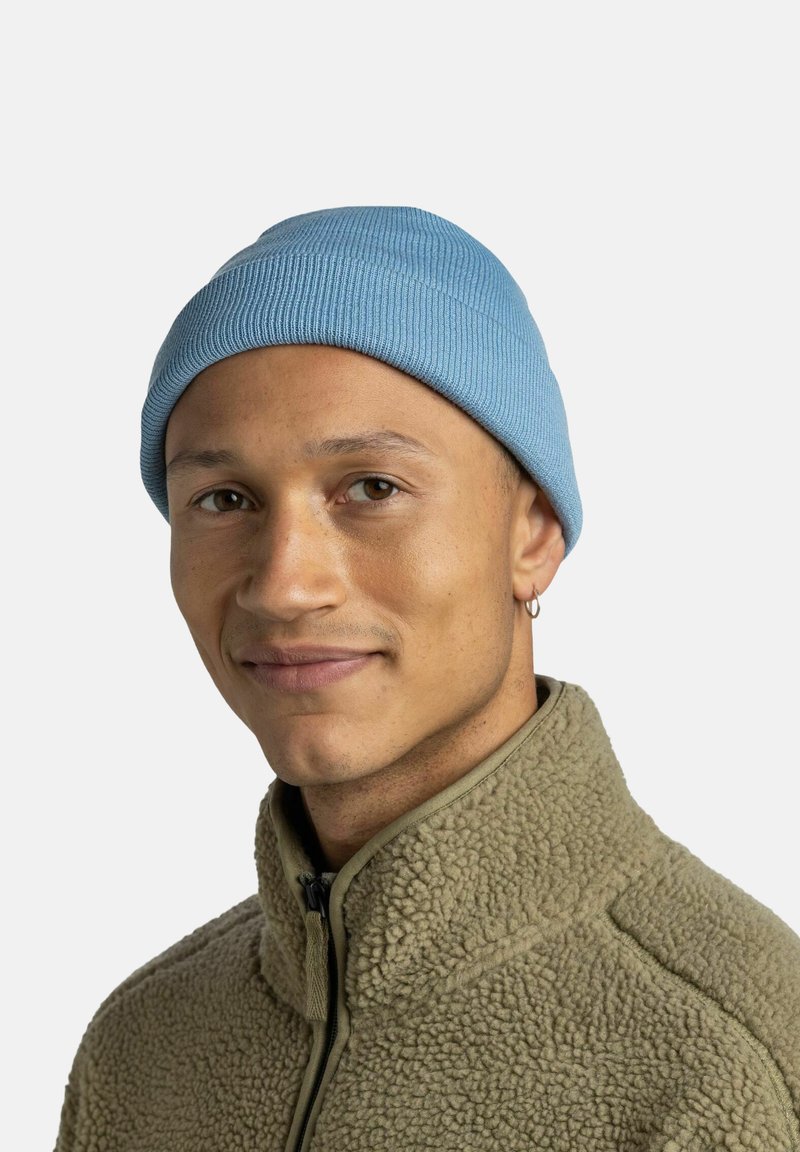 Light blue ribbed knit beanie atop an individual’s head, paired with a textured olive green fleece jacket featuring a high collar.