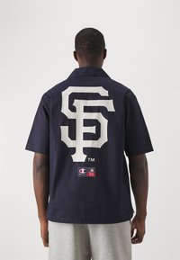 Marineblauwe shirt met korte mouwen en groot wit "SF" logo op de achterkant. Vermelding van Champion-label en MLB-tag aan de onderrand. Van katoen.