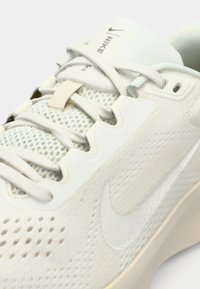 Αθλητικό παπούτσι Nike σε ανοιχτό κρεμ χρώμα με επάνω μέρος από δίχτυ και συνθετικό υλικό, με υφή στο πέλμα και εμφανές λογότυπο στο πλάι.