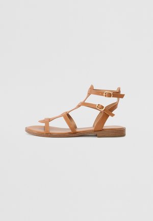 Sandálias de couro castanho com múltiplas tiras, altura até ao tornozelo, e duas fechos com fivela ajustável, apresentando uma sola plana e um design minimalista.