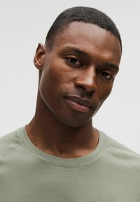 Light green short-sleeve shirt with a textured pattern, round neckline, and raglan sleeves, worn by a person with short hair.