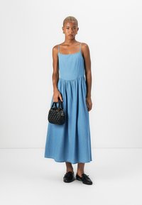 Denim maxikjole, lys blå, uten ermer med tynne stropper, rynket midje. Svart teksturert håndveske, svarte slip-on sko uten hæler.