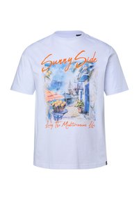 Camiseta blanca con un estampado colorido de una calle mediterránea junto al mar, que muestra una cesta de limones y el texto "Sunny Side" y "Living The Mediterranean Life".