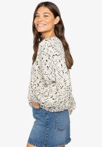 Gebreide trui in off-white met zwarte spikkels, met een boxy pasvorm en elastische mouwen, gecombineerd met een denim mini-rok.
