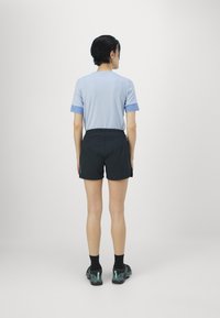 Lys blå kortermet skjorte med kontrasterende blå mansjetter, kombinert med svarte shorts og mørke joggesko med grønne detaljer.