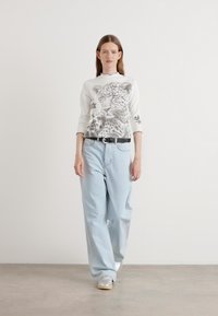 Witte lange mouwen shirt met een luipaardprint, gecombineerd met lichtblauwe wijdvallende spijkerbroeken en zilveren sneakers. Zwarte riem accentueert de taille.
