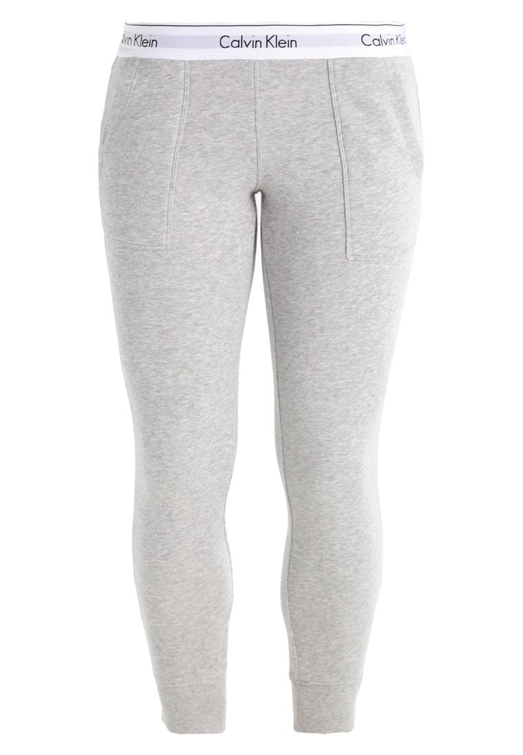 Pantalon de jogging gris avec une ceinture élastique blanche portant le logo "Calvin Klein", coupe fuselée et poches latérales. Tissu doux et texturé.