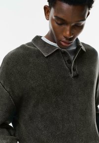 Donkergroene gebreide pullover met een kraagontwerp, knopenrij en textuurstof toont een close-up van de kraag en halslijn.