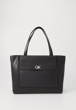 Sort lædertaske med dobbelte håndtag og frontlomme med sølv CK-logo på en neutral baggrund.