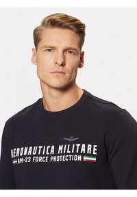 Felpa in cotone blu navy con colletto tondo, caratterizzata da un logo e testo stampati in bianco. Include un dettaglio a strisce verde, bianco e rosso.