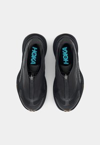 Baskets de course noires avec une tige texturée, fermeture éclair, et un logo "HOKA" bleu vif sur les semelles intérieures. Semelle extérieure Vibram pour une meilleure adhérence.