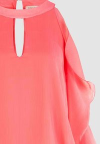 Blusa rosa trasparente con colletto alla coreana, apertura frontale a goccia e maniche ampie. Il tessuto strutturato aggiunge interesse visivo.