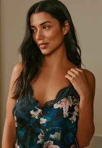 Saténové tielko s kvetinovým vzorom v tmavomodrej farbe, s krajkovým lemovaním so zvlneným okrajom a jemnými detailmi. Hladká textúra, ľahká látka.