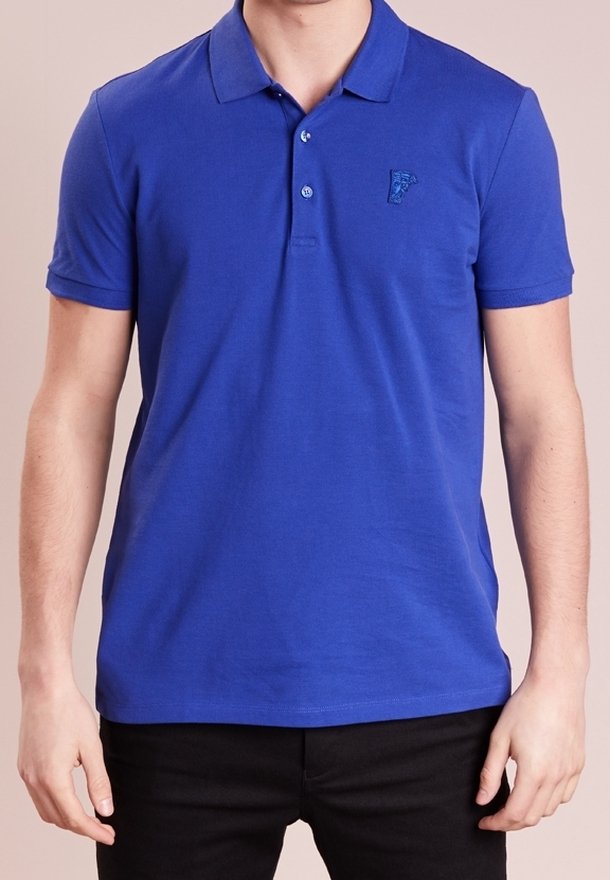 Homme portant un polo bleu à manches courtes avec un petit logo brodé sur la poitrine gauche et un pantalon noir.