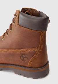 Stivaletto in pelle marrone con lacci, colletto imbottito scuro, suola strutturata e logo ad albero embosso sul lato.