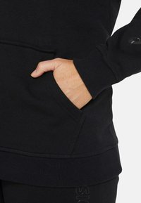 Black sweatshirt featuring a kangaroo pocket, ribbed cuffs, and hem. Soft fabric with an embroidered logo on the sleeve.