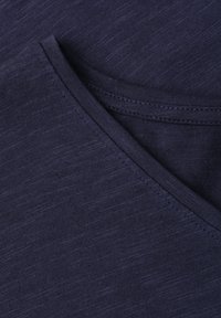 Gros plan d'un tissu bleu marine avec une couture détaillée sur un bord plié, montrant la texture et la construction de la couture.