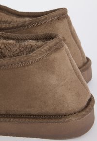 Chaussons en suede marron avec doublure en fausse fourrure, présentés de dos sur un fond blanc.