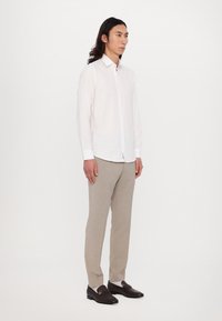 Weißes Langarmhemd, beigefarbene Hose, dunkelbraune Mokassins mit Logodetail. Glattes Material, taillierte Passform mit Button-Down-Kragen.