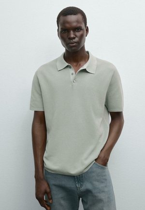 Polo-shirt à manches courtes de couleur vert clair avec une finition texturée, patte de boutonnage à trois boutons et col classique, associé à un jean en denim.