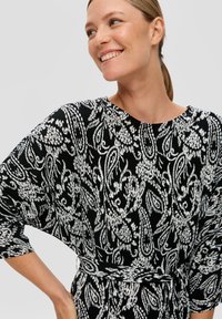 Zwart-wit gestippeld jurk met een losse pasvorm, voorzien van een riem in de taille, brede mouwen en een ribbelstructuur.