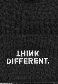 Čierna pletená čiapka s rebrovanou textúrou, na ktorej je výrazne vyšitý biely text "THINK DIFFERENT." na prednej strane.