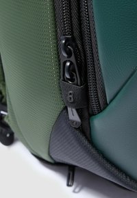 Zaino verde con tessuto strutturato, dettagli in pelle liscia e una cerniera nera con una linguetta unica per una chiusura sicura.