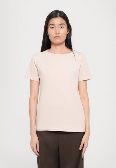 T-shirt rose clair à manches courtes, col rond, en tissu doux, coupe droite, associé à un pantalon large marron. Design simple et minimal.