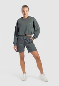 Sweat-shirt court vert foncé avec ourlet côtelé, associé à un short taille haute assorti avec poches latérales. Des baskets blanches complètent la tenue.