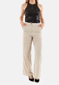 Top senza maniche nera con una texture lucida, abbinata a pantaloni a gamba larga beige chiaro a righe, dotati di due tasche frontali e chiusura con bottone.