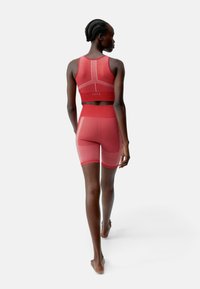 Rotes Sportset bestehend aus einem figurbetonten Sport-BH und Shorts bis zur Mitte des Oberschenkels. Das Material hat eine glatte Textur mit kontrastierenden weißen Nähten und Akzenten.