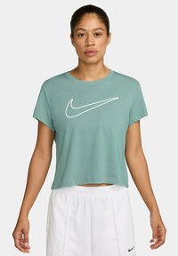 T-shirt verde cropped con collo rotondo e maniche corte; presenta un grande logo Nike bianco sul davanti. Materiale in cotone morbido.