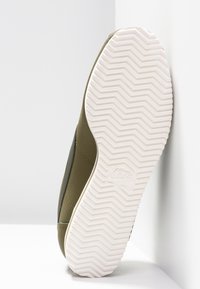 Olivově zelené tenisky s texturovaným svrškem, bílou gumovou podrážkou a cik-cak vzorem. Obsahují logo Nike na boku a jemné švy.