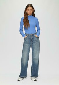 Lichtblauw geribbeld langetermijntop met een hoge nek, gecombineerd met een brede licht denim jeans met een vervaagde wash en rafelige zoom. Witte sneakers.