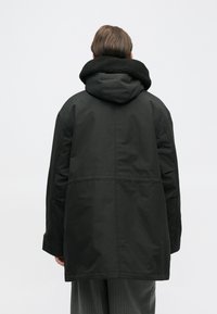 Must mustaga, millel on pehme karvaga kaelus, laiem lõige, pikad varrukad ja üks keskmine õmblus seljaosas.