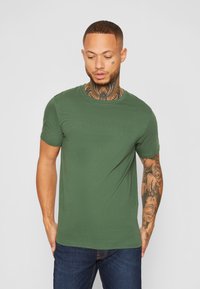 Grünes T-Shirt mit kurzen Ärmeln aus weicher Baumwolle, mit Rundhalsausschnitt und schlanker Silhouette, kombiniert mit dunklen Jeans.