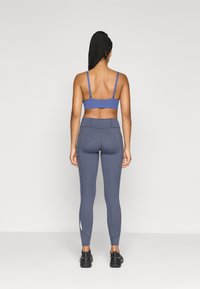 Zila sporta krūšturis un pelēki legingi ar šauru piegriezumu, vertikālām baltām akcentiem, gludu tekstūru un elastīgu materiālu. Melni sporta apavi.