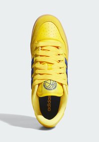 Baskets Adidas jaunes avec des rayures bleues, lacets jaunes, boîte à orteils perforée et logo de basketball sur la languette, vu de dessus.