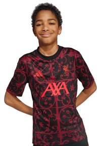 Camisa del Liverpool FC en negro y rojo con un patrón floral, cuello redondo, mangas cortas y el prominente logo de AXA en rojo.