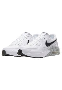 Witte sportieve schoenen van gaas en leer, met een zwarte Nike swoosh, gestructureerde tussenzool en zwarte buitenzool.