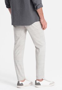 Pantaloni a quadri grigio chiaro con vestibilità slim, caratterizzati da una texture sottile e un tessuto liscio. Abbinati a sneakers bianche con accenti grigi.